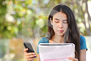 Teenager student girl looking sideways at mobile phone while studying photo