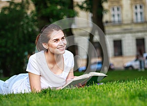 Teenager student girl lying on grass in park near university reading book outdoors