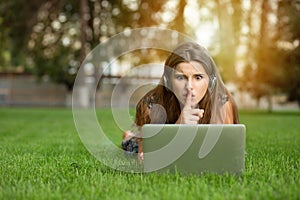 Teenager student working on a laptop making hush sign outdoors