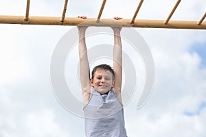 A teenager in a T-shirt is engaged in gymnastics on a horizontal bar