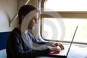 A teenager in a train compartment at the window works in a laptop. Russian Railways. Modern technologies