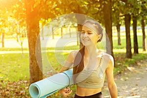 Teenager training in nature, young athletic woman goes to do sports with a yoga mat and fitness exercises in the park, healthy