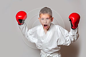 A teenager in a white kimono and gloves for hand-to-hand combat on a gray background. Doing sports