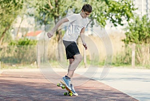 Teenager in white t shirt spends free time training skating in the city park. Practicing skills freestyle, making tricks.