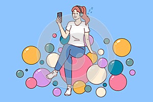 Teenager woman listening to music on headphones and holding mobile phone sitting on balloons