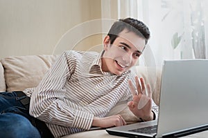 Young man lying on sofat and using laptop at home