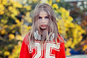 Teenager young woman blonde girl, long hair blue eyes headphones around neck red shirt 25 on it looking at you camera serious