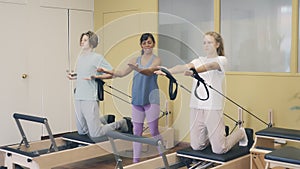 Teenagers boy and girl practicing Pilates system on reformer supervised in gym