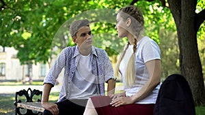 Teenagers couple conflicting, sitting at park bench, conflict based on jealousy