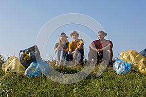 Teenagers have collected plastic trash bags and sit on the hillock