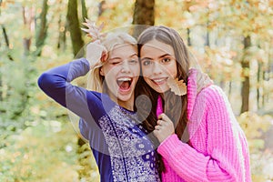 Teenagers having fun on autumn background. Two Surprise woman playing with leaves and looking at camera. Happy young