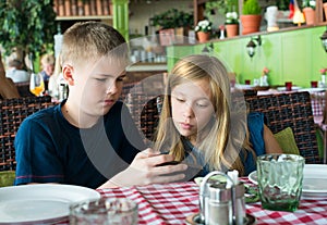 Teenagers having fun with mobile phones in cafe. Modern lifestyle and technology concept. Children sitting in restaurant and