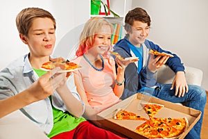 Teenagers holding pizza pieces and eating