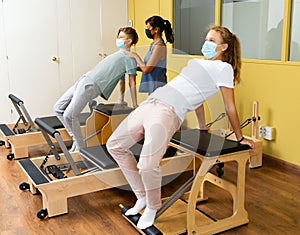 Teenagers in masks training pilates in gym with traine