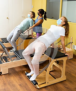 Teenagers in masks training pilates in gym with traine