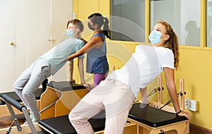 Teenagers in masks training pilates in gym with traine