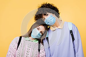 Teenagers in medical masks looking at camera isolated on yellow.