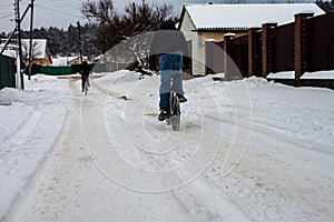 Teenagers ride bicycles on a snowy road in winter