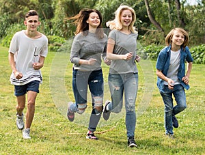 Teenagers running through green lawn in summer in park