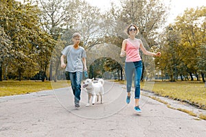 Teenagers running with white dog Husky on the road in the park