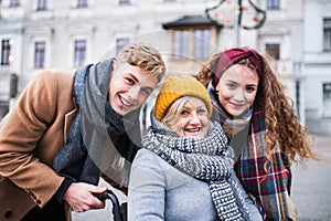 Teenagers and senior grandmother in wheelchair on the street in winter.