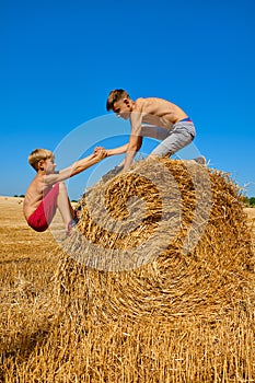 Teenagers in shorts and with an open torso jump on haystacks. Blue sky. Friends having fun outdoors.