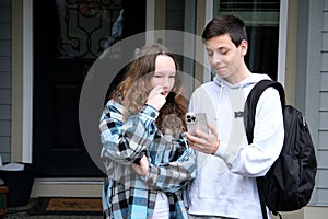 teenagers show interesting news boy and girl with briefcase phone at door at home Smiling couple looking in smartphone