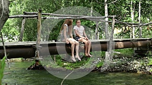Teenagers sits on a narrow wooden bridge over a mountain river. camping and adventure concept