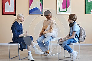Teenagers sitting in circle while discussing art in modern art gallery or museum
