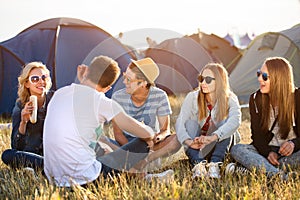 Teenagers sitting on the ground in front of tents, eating