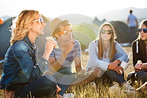 Teenagers sitting on the ground in front of tents and eating