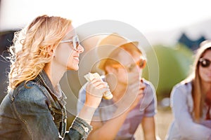 Teenagers sitting on the ground in front of tents and eating