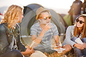 Teenagers sitting on the ground in front of tents, resting