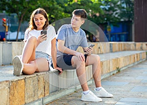 Teenagers with smartphones are siting on the step