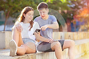 Teenagers with smartphones are siting on the step