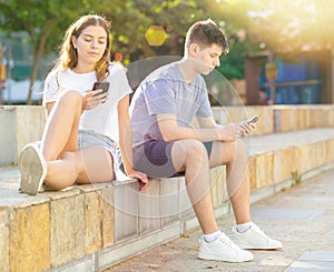 Teenagers with smartphones are siting on the step