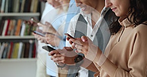 Teenagers standing indoor with smartphones in hands, closeup cropped view