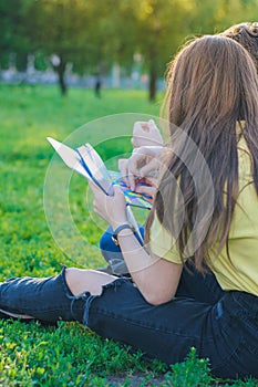 Teenagers studying together and lerning notes on the green lawn near college