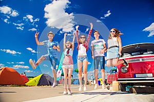 Teenagers at summer festival jumping by vintage red campervan
