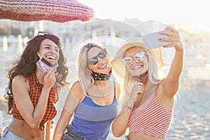 Teenagers taking a selfie in beach - Young girls smiling in front of the camera with face mask on - The new coronavirus lifestyle