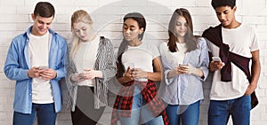 Teenagers texting on their smartphones, leaning on wall