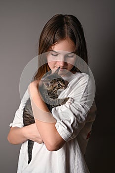 Teengirl holding a baby cat on gray background. Kitten sits on the female shoulder. Vertical photo. Side view