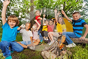 Teens with arms up near bonfire hold marshmallow