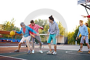 Teens boys playing basketball on outdoor court, playground and having fun