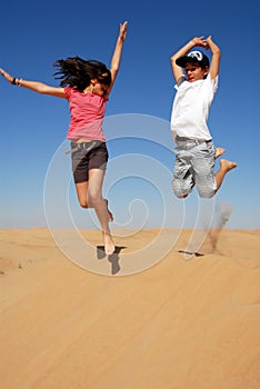 Teens joyfully leaping in desert dunes under a blue sky, reveling in playful moments and boundless enjoyment