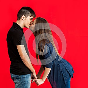 Teens kissing against red backdrop.