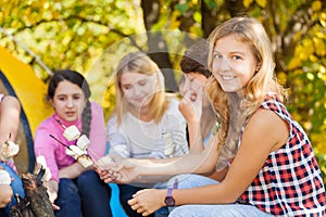 Teens sit on campsite with marshmallow sticks