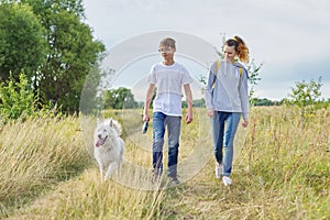Teens walking with white dog in meadow on sunny day