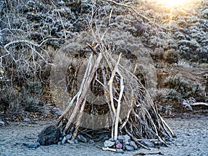 Teepee structure for shelter made of tree branches on a sandy beach in the Nevada desert.