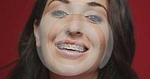 Teeth alignment by braces. Female smiling on red studio background. Dental care, stomatology, orthodontic treatment